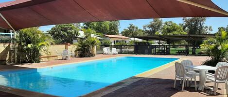 Una piscina con zona sombreada, sillas de descanso y una mesa.