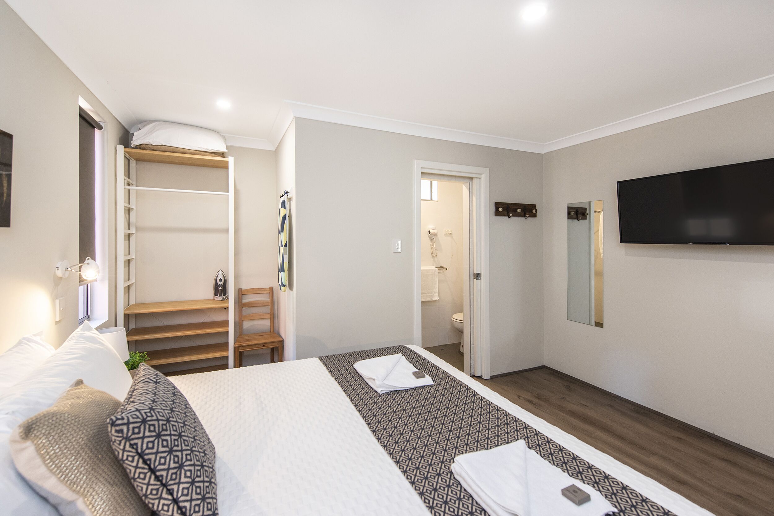 Habitación de hotel con cama, televisor, armario y baño visible a través de una puerta abierta.