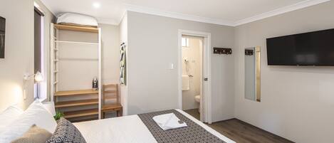 A hotel room with a bed, a TV, a wardrobe, and a bathroom visible through an open door.