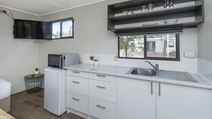 Une cuisine de taille réduite, avec des meubles blancs, un four à micro-ondes, un évier et une fenêtre donnant sur l’extérieur.