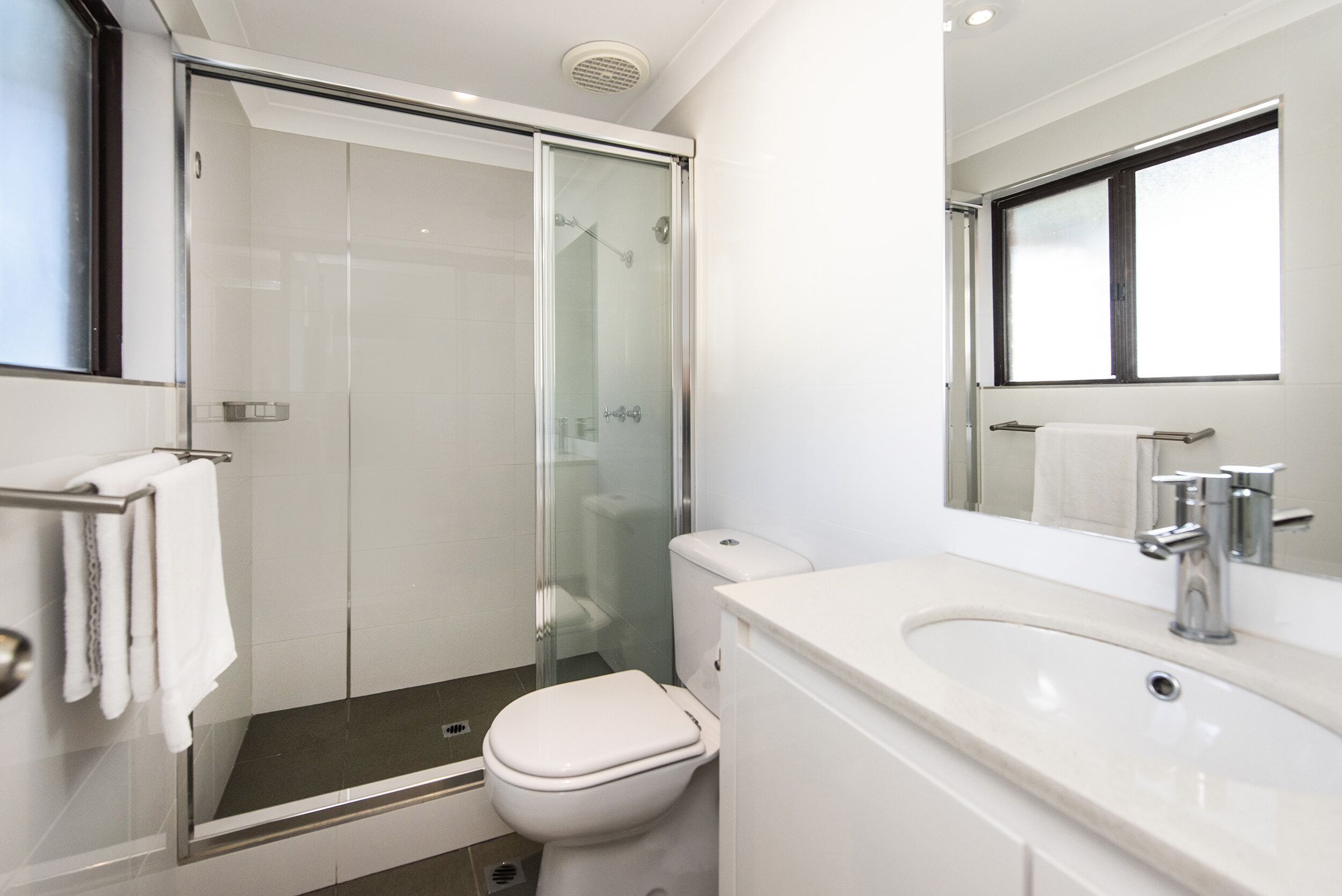 A modern bathroom with a glass-enclosed shower, a white toilet, and a sink with a mirror above it.
