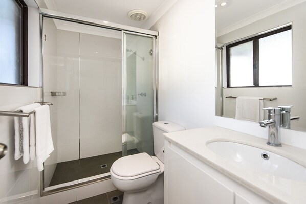 A modern bathroom with a glass-enclosed shower, a white toilet, and a sink with a mirror above it. - Banksia Tourist Park (Hazelmere)