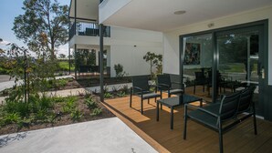 Un espace extérieur moderne, aménagé avec une terrasse en bois, des chaises en métal et un mur de verre offrant une vue sur le paysage environnant.