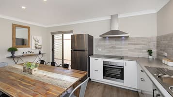 A modern kitchen with a wooden dining table, stainless steel appliances, and a tiled backsplash.