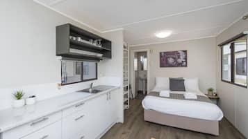 A compact hotel room with a kitchenette, a bed with white bedding, a small bedside table, and a window with a view.