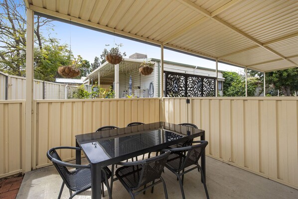 A covered patio with a table and chairs, a decorative fence, and hanging baskets. - Banksia Tourist Park (Hazelmere)