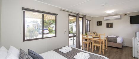 A hotel room with a bed, a dining table with chairs, a sofa, and a refrigerator.