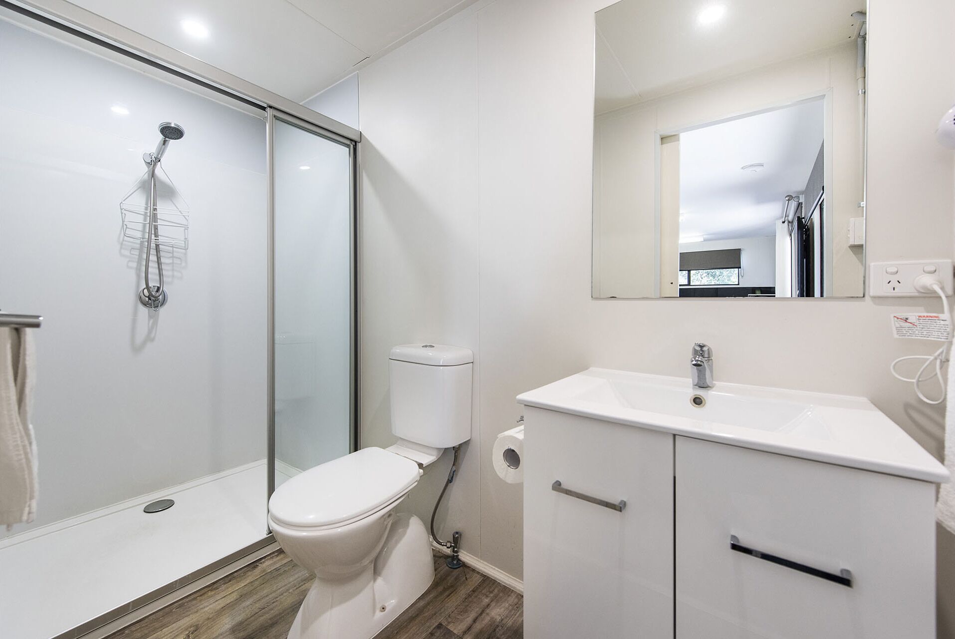 A modern bathroom with a glass shower enclosure, a white toilet, and a white sink with a mirror above it.