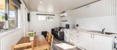 A compact kitchen with white cabinets, a wooden dining table, and a built-in microwave.