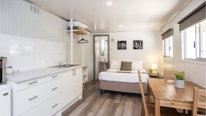Une pièce compacte comprenant un coin cuisine, un lit, une table de chevet avec une lampe et une fenêtre.