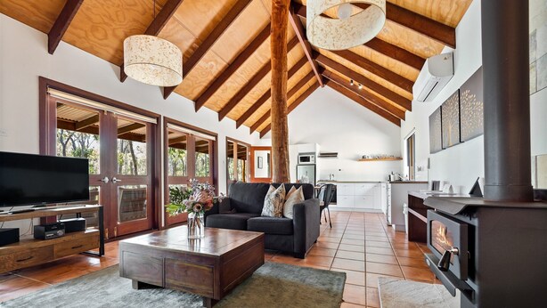 A spacious living area with a high ceiling, wooden beams, a fireplace, and a kitchen in the background. - Forest Rise (Yelverton)