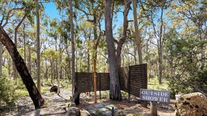 A wooden bench and a sign reading "OUTSIDE SHOWER" in a forested area with a stone pathway. - Forest Rise (Yelverton)