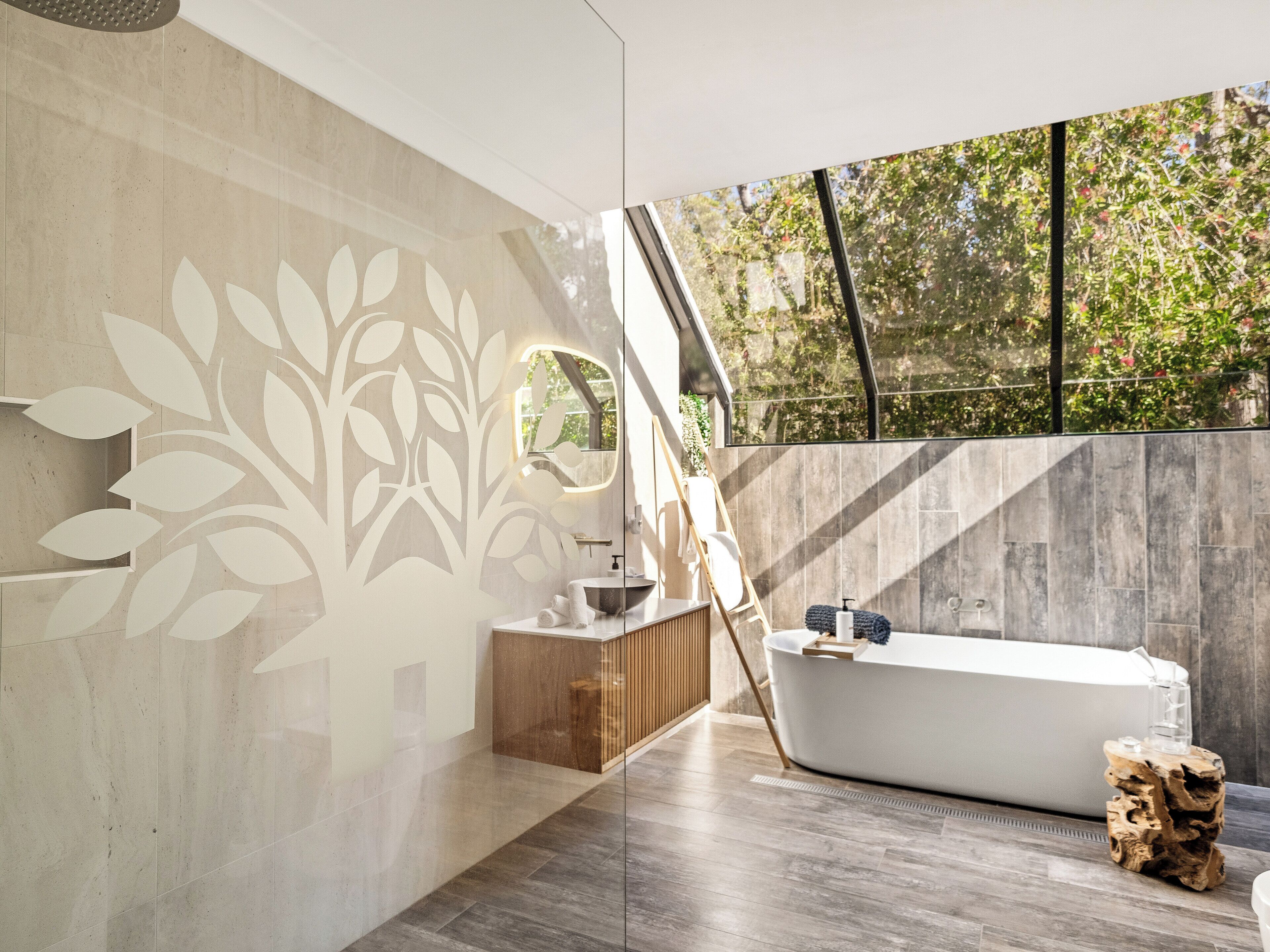 A modern bathroom with a freestanding bathtub, a wooden vanity, and a large window offering a view of trees.