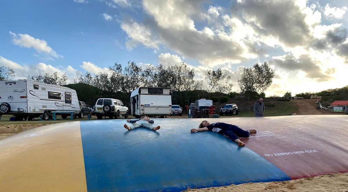 A recreational area with a trampoline, RVs, and a dirt path.