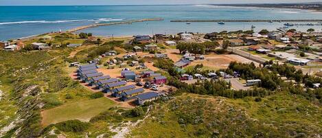 Una vista aerea di una zona costiera con file di cabine alimentate a energia solare, un molo che si protende verso il mare e edifici residenziali sparsi.
