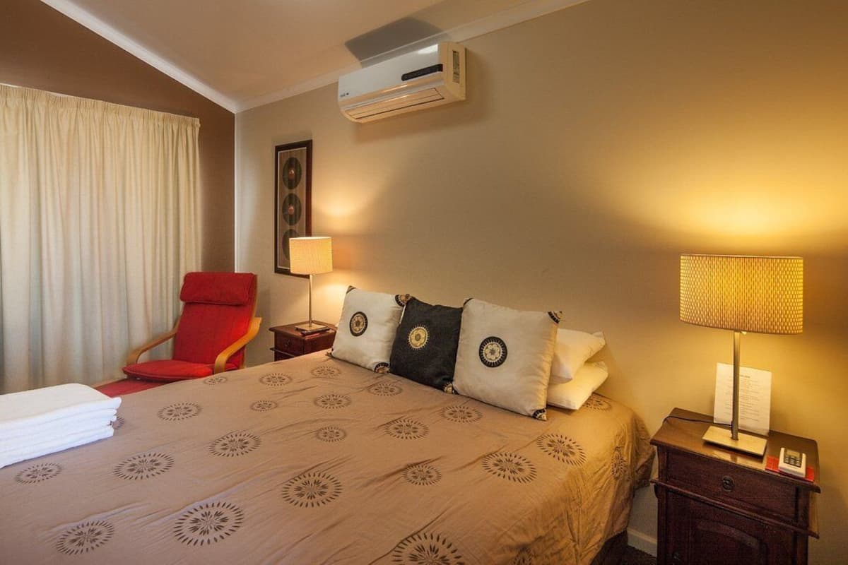 Ein Hotelzimmer mit einem Bett, einem roten Sessel, zwei Nachttischen mit Lampen, einer Klimaanlage und einem Fenster mit Vorhängen.