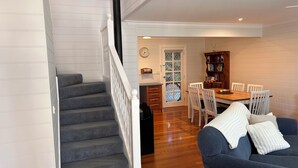 A staircase leading to a dining area with a wooden table and chairs, a clock on the wall, and a bookshelf. - Dunes - elegant beach villa with huge swim spa (Port Fairy)