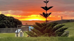 A house with a small garden, a fence, and a sunset in the background. - Dunes - elegant beach villa with huge swim spa (Port Fairy)