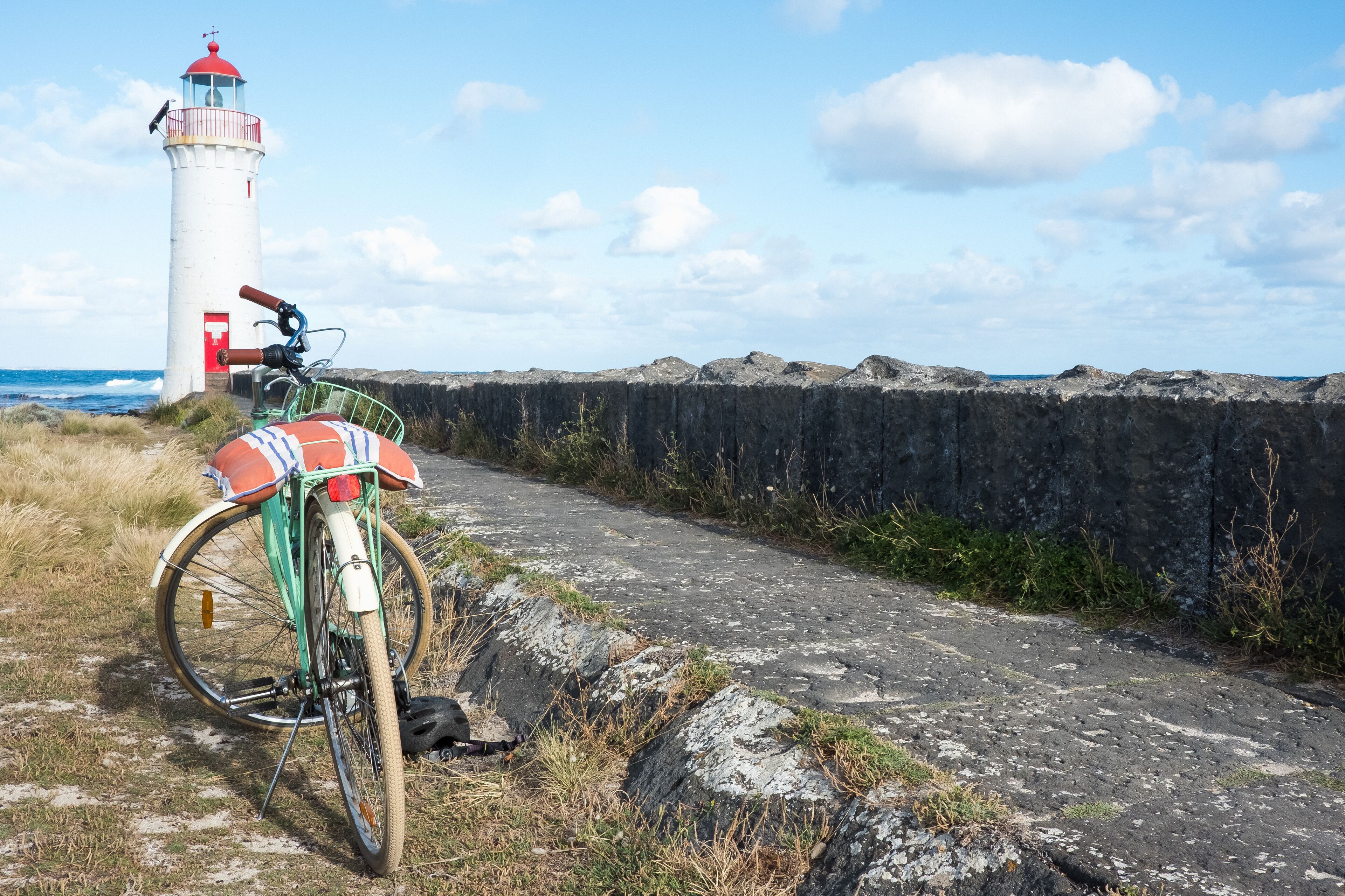A bicycle parked on a coastal path with a lighthouse in the background.