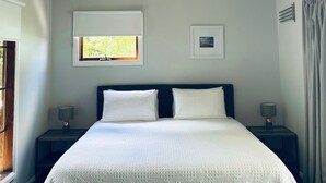 Un dormitorio con una cama, dos mesitas de noche, un ventanal y un techo con diseño geométrico.