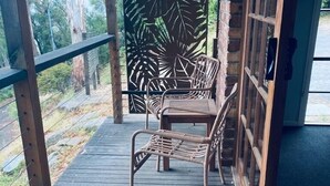 Una terraza de madera con dos sillas de mimbre y un panel decorativo con diseños de hojas.