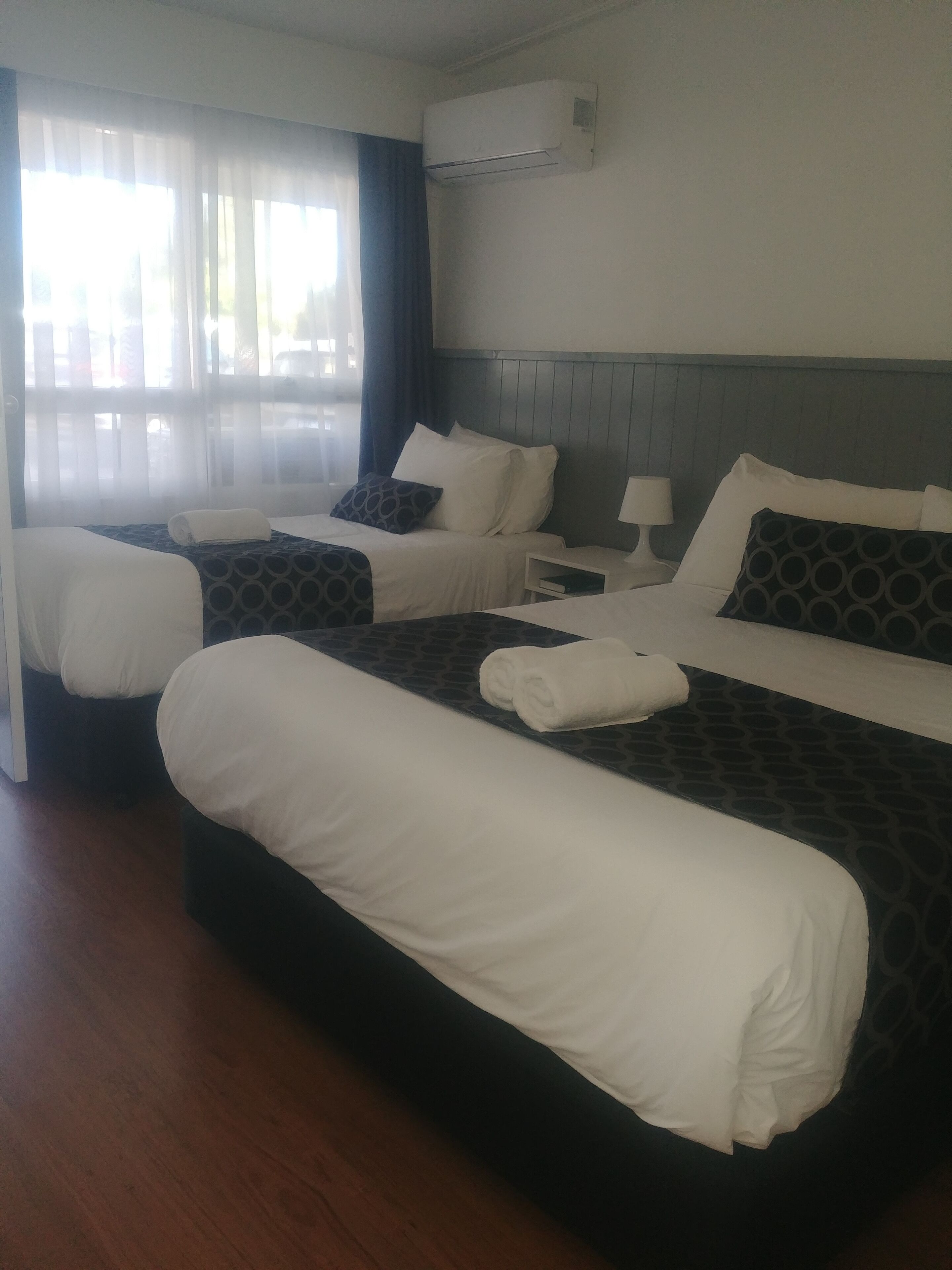 A hotel room with two beds, a nightstand, a lamp, and an air conditioning unit.