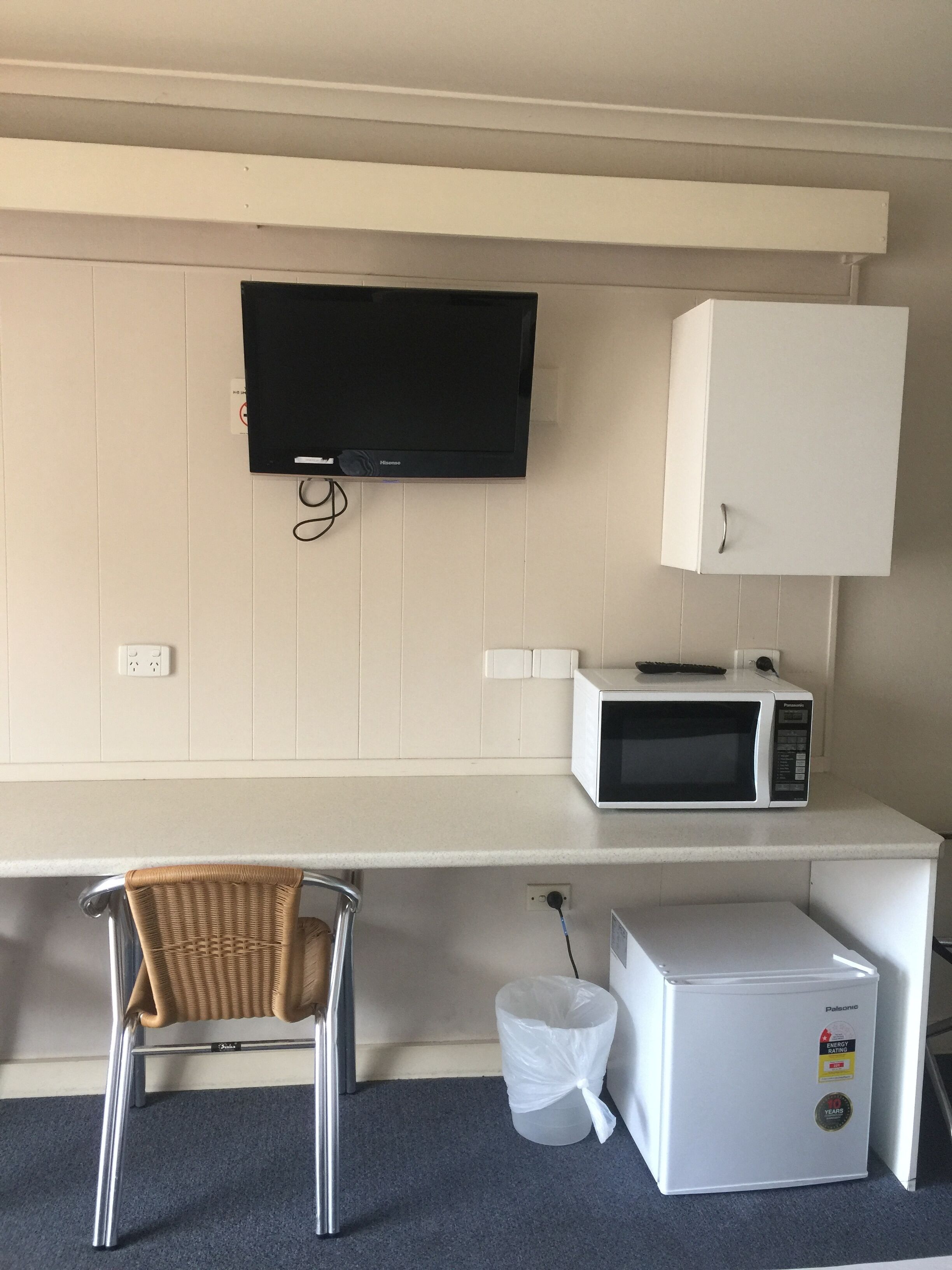 Una kitchenette con televisión de pantalla plana, microondas, refrigerador y una silla de mimbre.