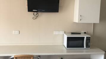 Una kitchenette con televisión de pantalla plana, microondas, refrigerador y una silla de mimbre.
