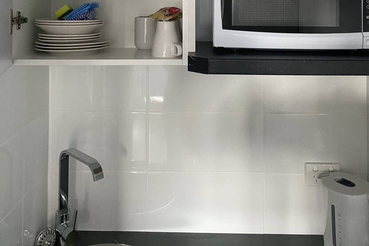A kitchen with white cabinets, a microwave, a kettle, and a sink.