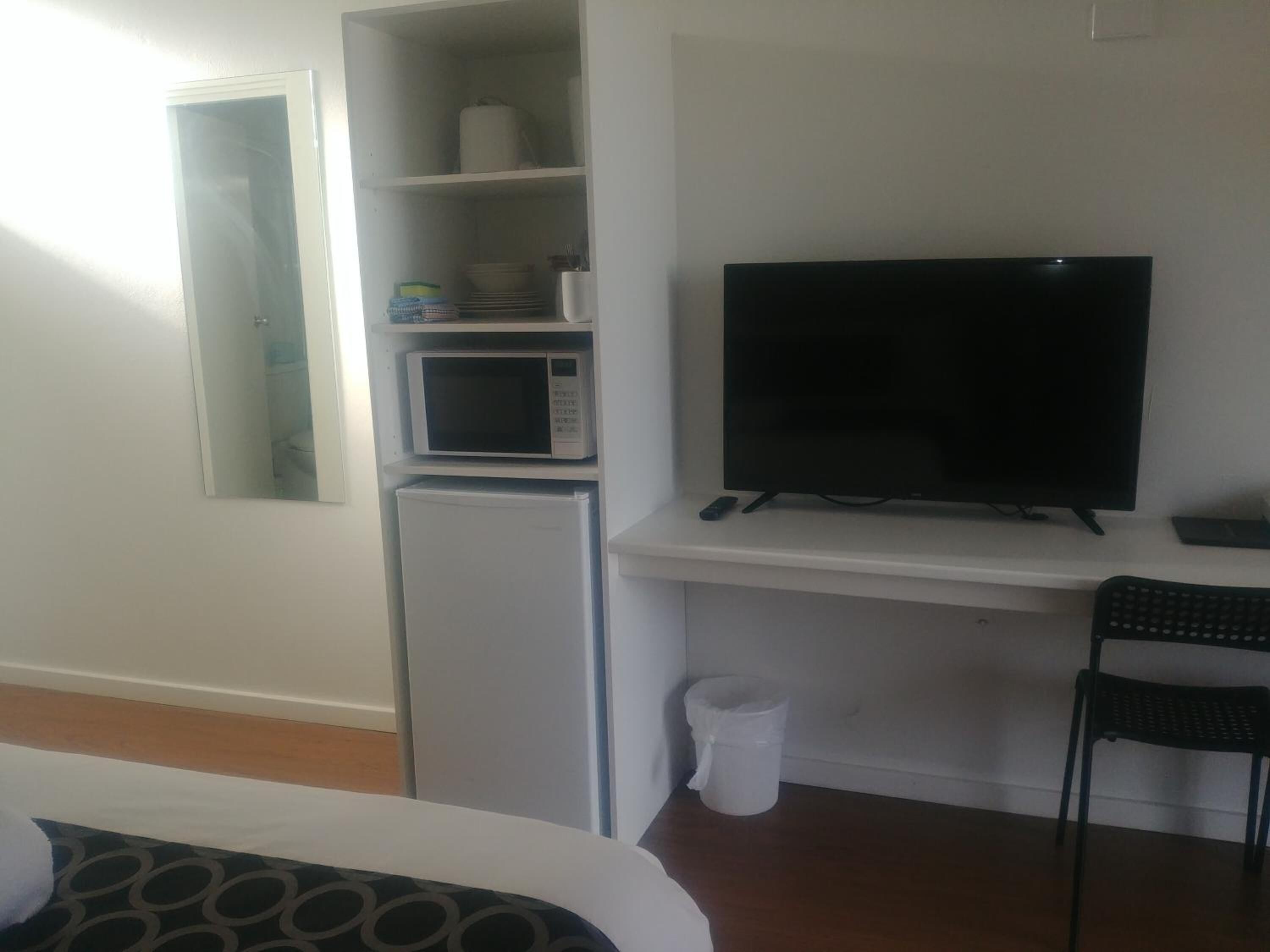 Ein kleines Hotelzimmer mit einem Bett, einer kompakten Küchenzeile inklusive Mikrowelle und Kühlschrank, einem Fernseher und einem Sessel.