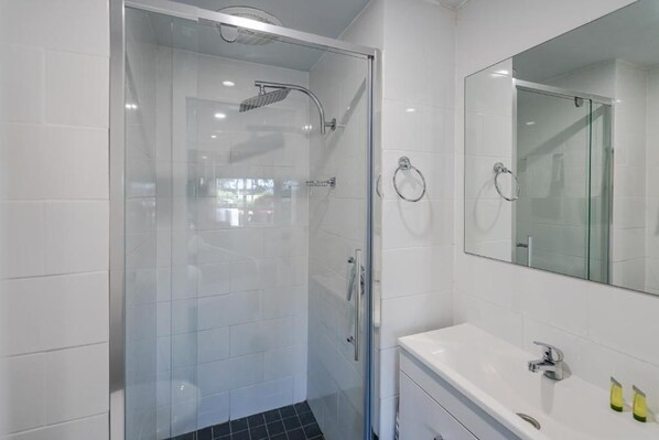 A modern bathroom with a glass-enclosed shower, a white sink, and a mirror above the sink.