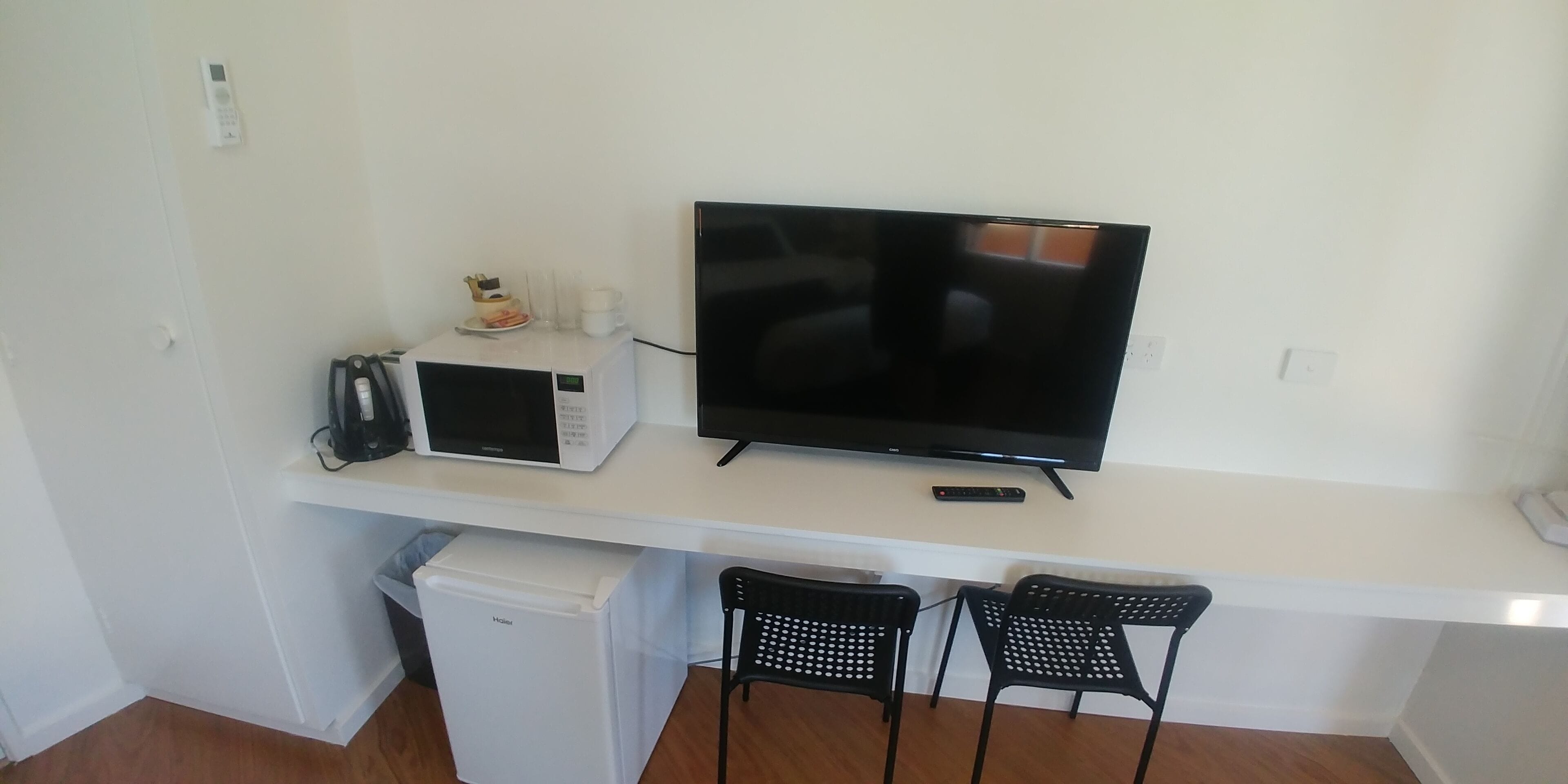 A compact living space with a flat-screen TV, a microwave, a small refrigerator, and two black chairs.