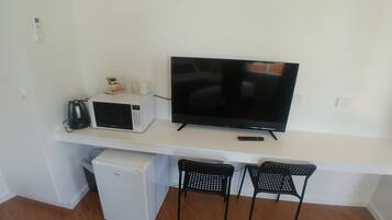 A compact living space with a flat-screen TV, a microwave, a small refrigerator, and two black chairs.