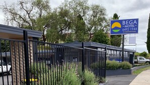 A gated entrance to BEGA MOTEL with a signboard, a paved pathway, and a grassy area with plants. - Bega Motel (Bega)