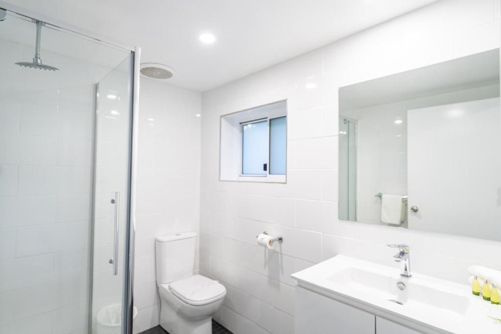A modern bathroom with a glass shower enclosure, a toilet, a sink with a mirror, and a window above the toilet.
