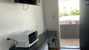A compact kitchen with a microwave, a small refrigerator, and a sink. There is a black countertop and a chair. The room has a door leading outside and a wall with a number. - Bega Motel (Bega)