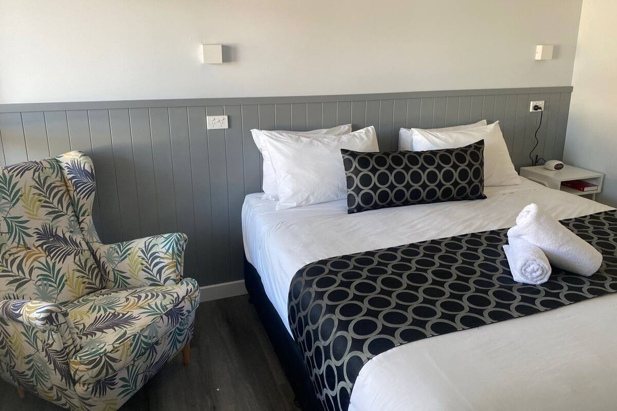A hotel room with two beds, a chair, and a nightstand.