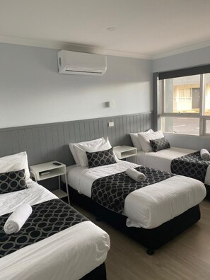 A hotel room with two single beds, a small bedside table with a lamp, and a large window providing a view of the street.