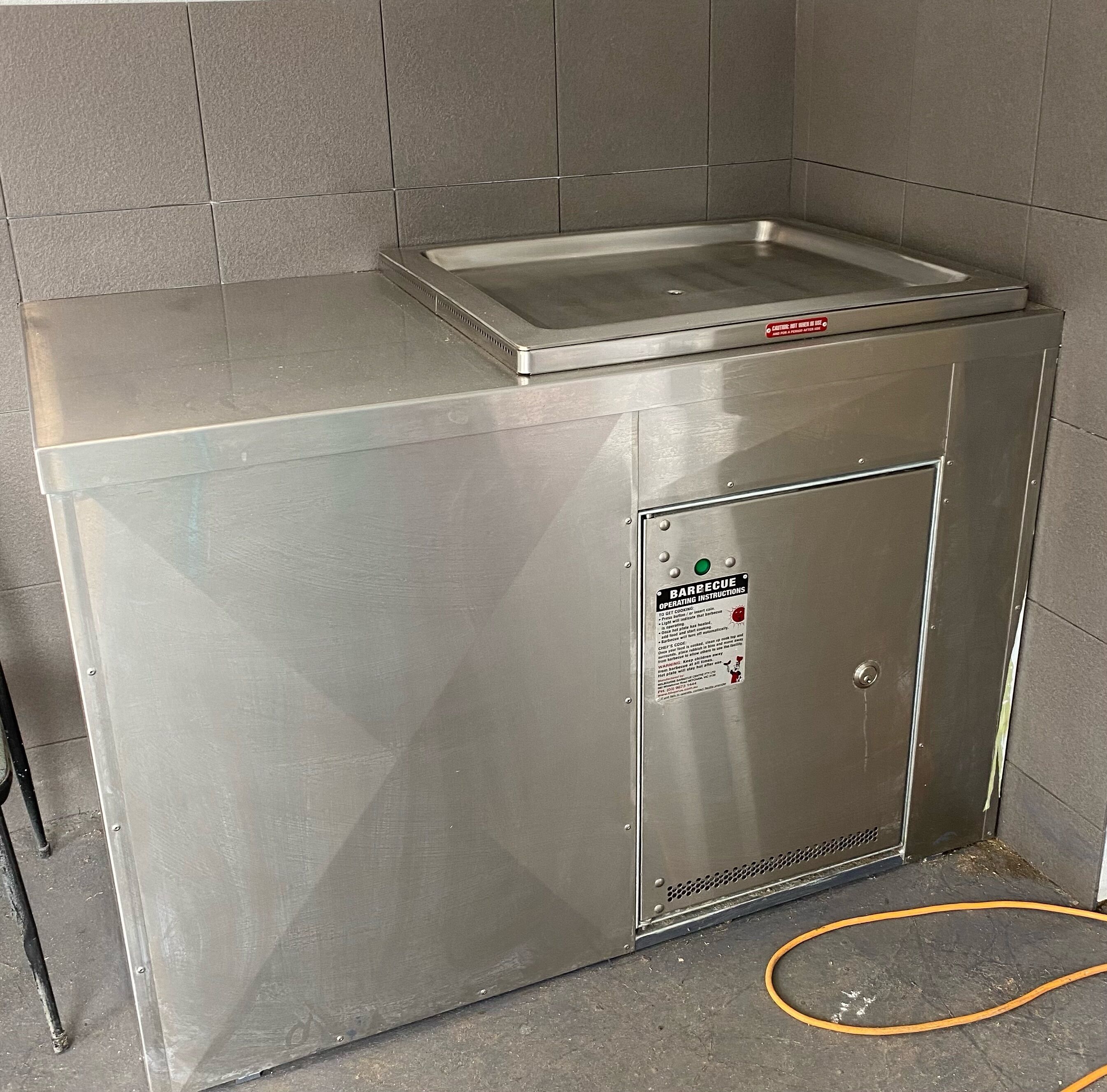 A stainless steel kitchenette with a built-in sink and a sign with operating instructions.