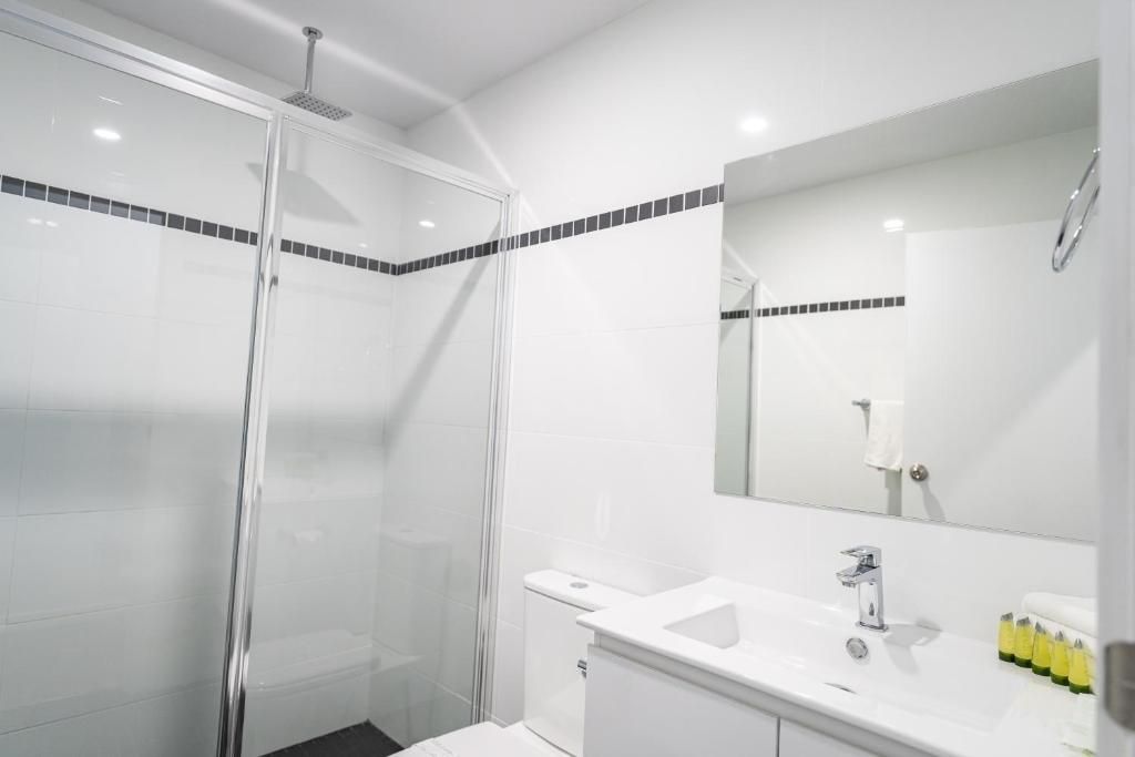 Un baño moderno con ducha acristalada, lavamanos blanco y espejo sobre él.