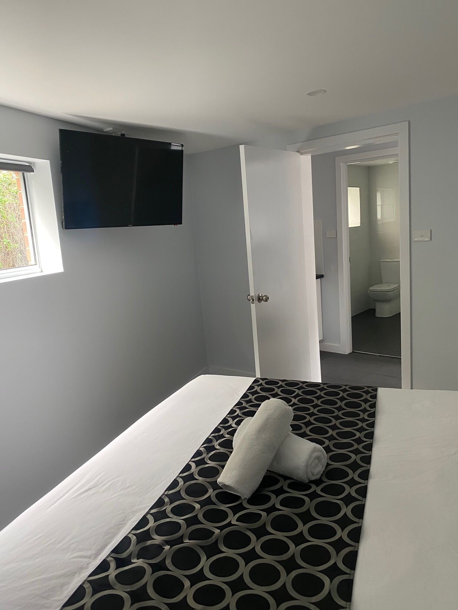 A hotel room with a bed, a TV mounted on the wall, and a bathroom visible through an open door.