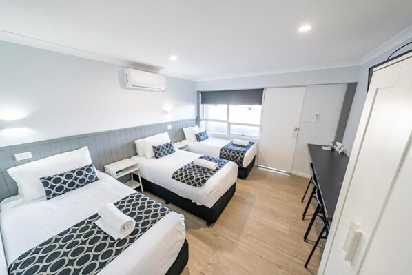 A hotel room with three beds, a desk, and a window.