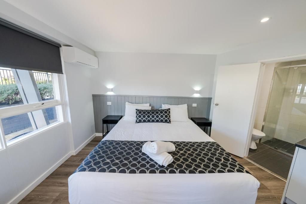Una habitación de hotel con cama, mesitas de noche, ventana y baño.