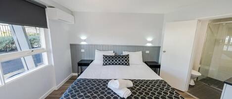 Una habitación de hotel con cama, mesitas de noche, ventana y baño.