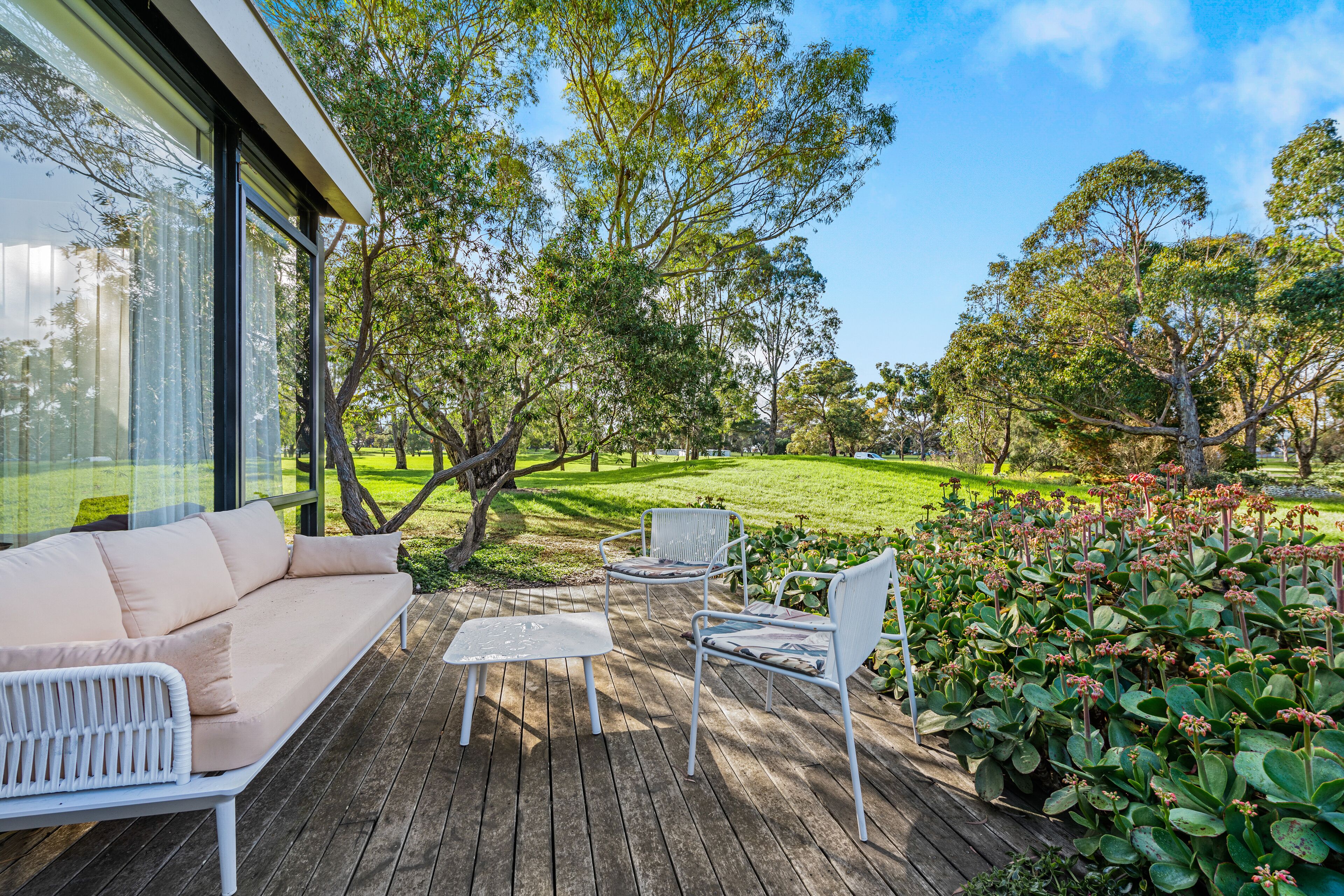 Une terrasse en bois avec un canapé et des fauteuils, entourée d’une végétation luxuriante et d’arbres.