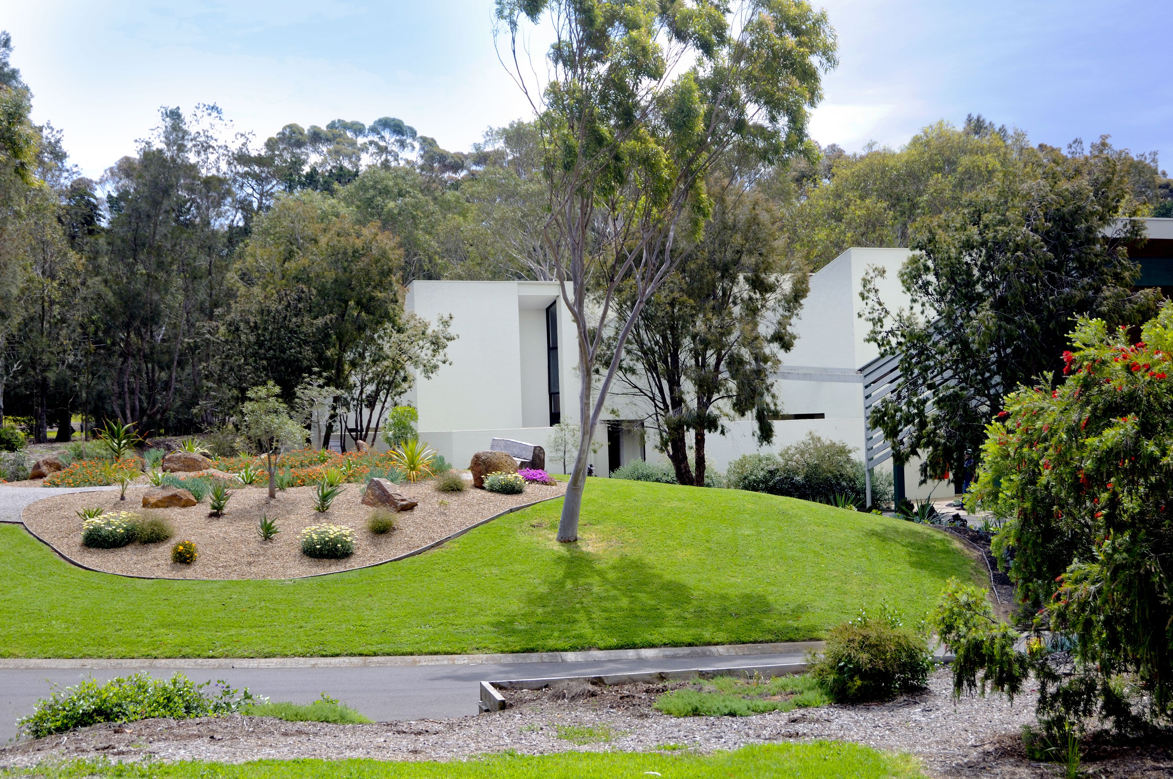 A modern building with a flat roof, surrounded by a landscaped garden with various shrubs and trees.