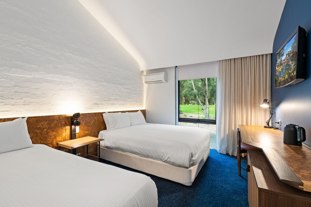 A hotel room with two beds, a desk, a TV, and a window with curtains.