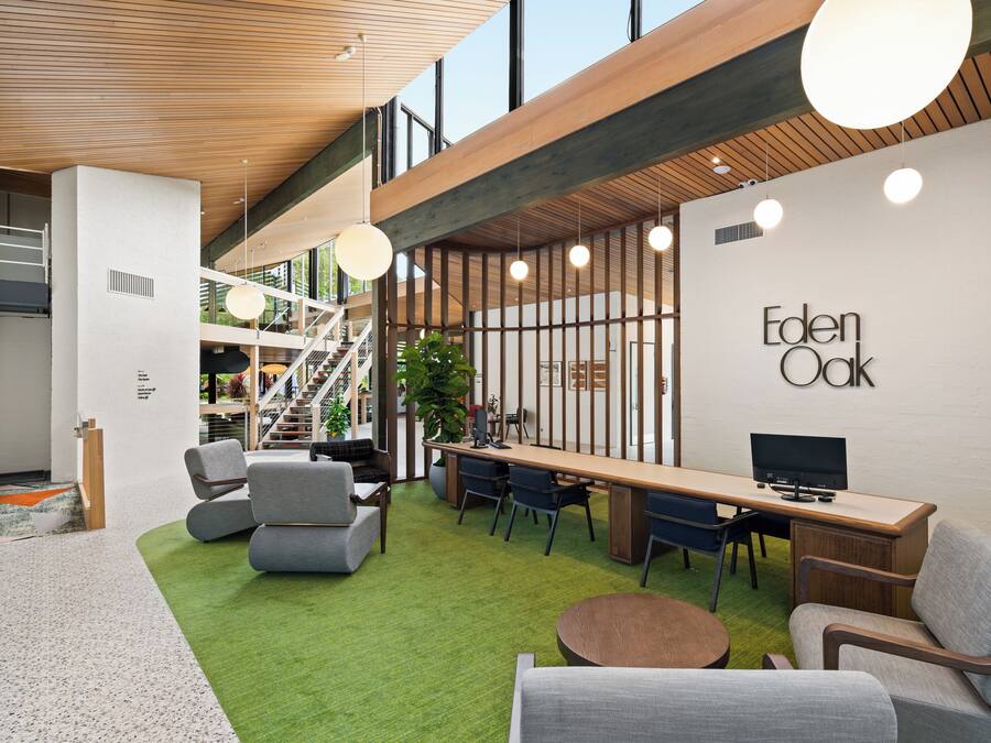 Um espaço de escritório moderno com teto de madeira, carpete verde e uma mesa comprida com cadeiras.