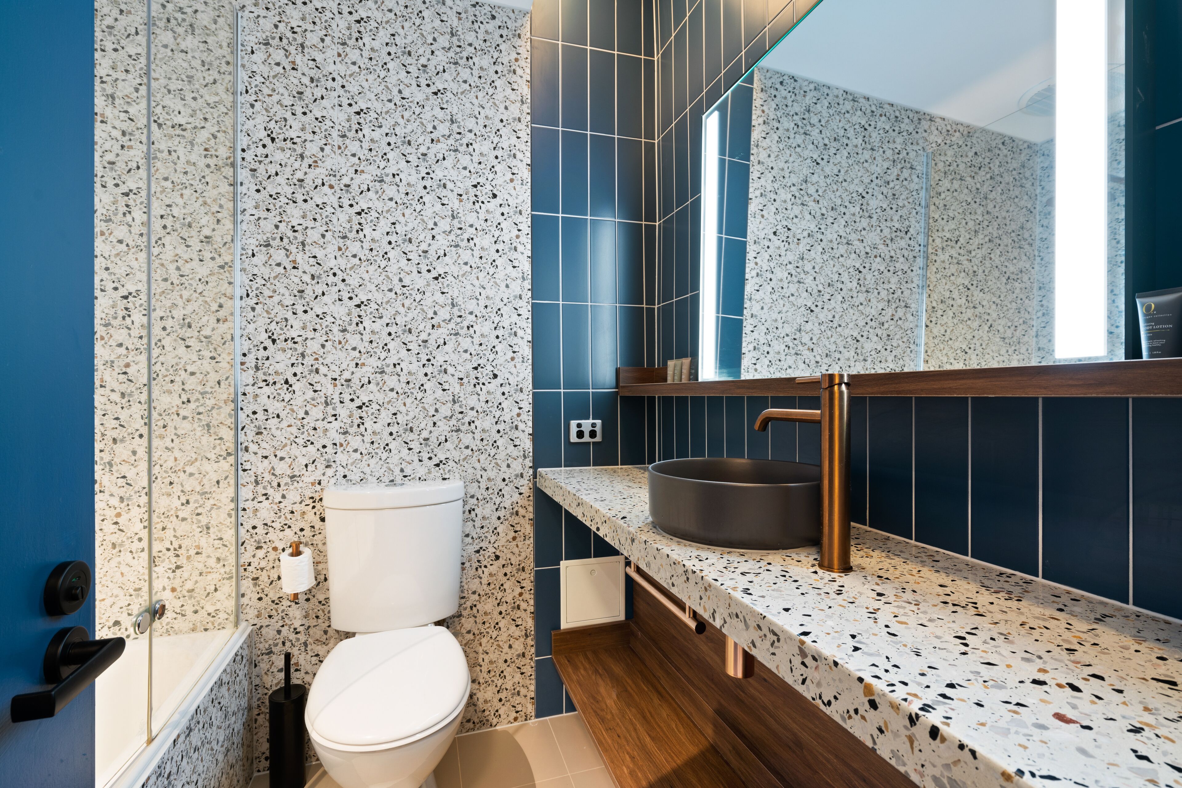 Un baño moderno con inodoro independiente, lavamanos con recipiente amplio y espejo sobre el lavamanos.