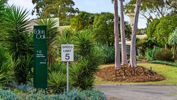 Una señal de límite de velocidad, un cartel verde con el texto 'Eden Oak' y una zona ajardinada con árboles y arbustos.
